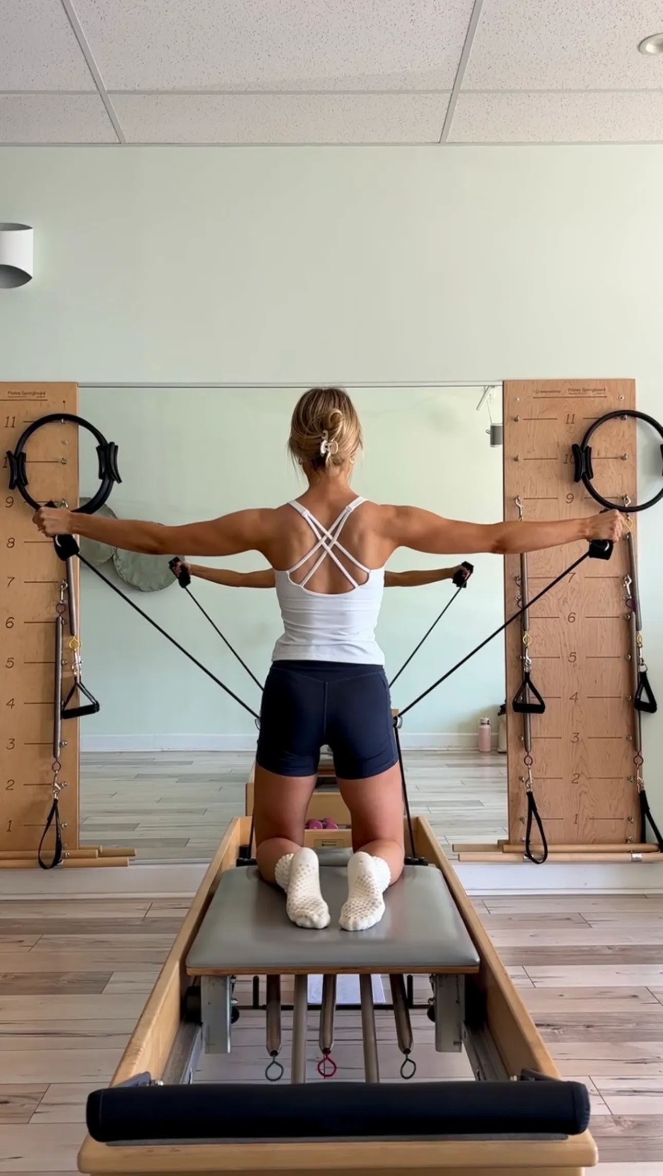 Charlotte on the Pilates reformer, arms extended wide in a strong, controlled position